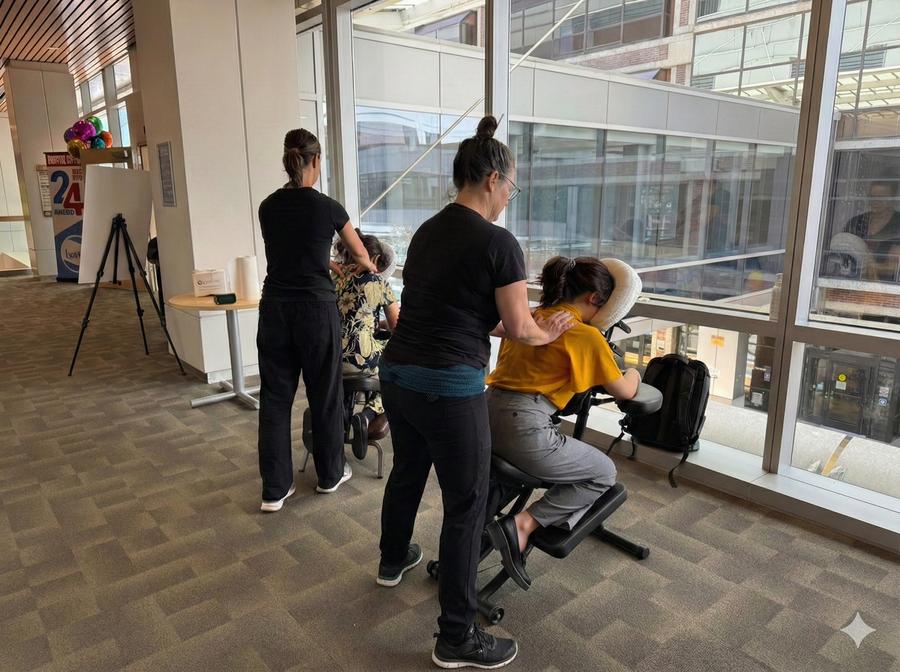 Licensed therapist providing chair massage to a seated client at a corporate wellness event